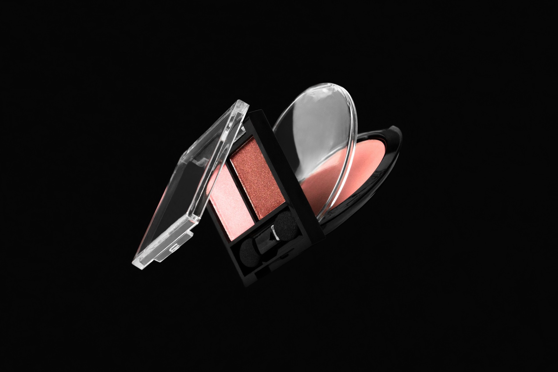 Flying makeup professional products for face on black background. Creative composition with pink eyeshadows and blusher. Fashion cosmetic beauty levitation in the air concept. Stock photo.