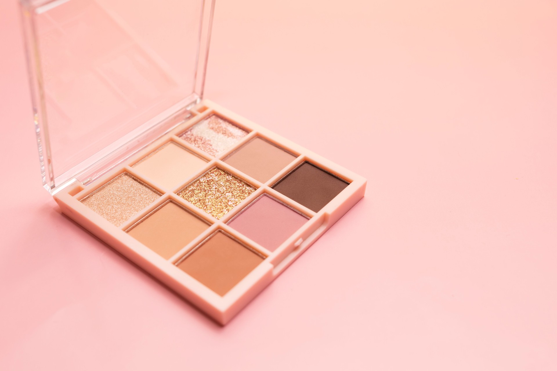 Eyeshadow palette cosmetics for eyes, face on pink background. Minimalism makeup, multicolored, delicate shades. Copy space for text on right side, horizontal. High quality photo